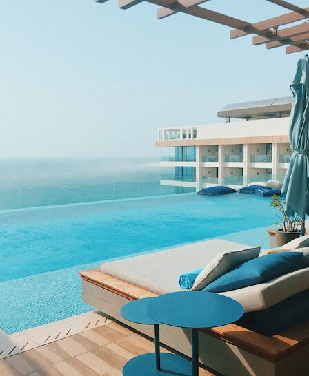 A luxurious poolside deck with lounge chairs, tables, and umbrellas overlooking a serene ocean view at a modern resort on a clear day.