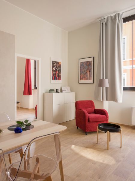 A modern living room with a red sofa, armchair and a dining table. A window with gray curtains lets in natural light.