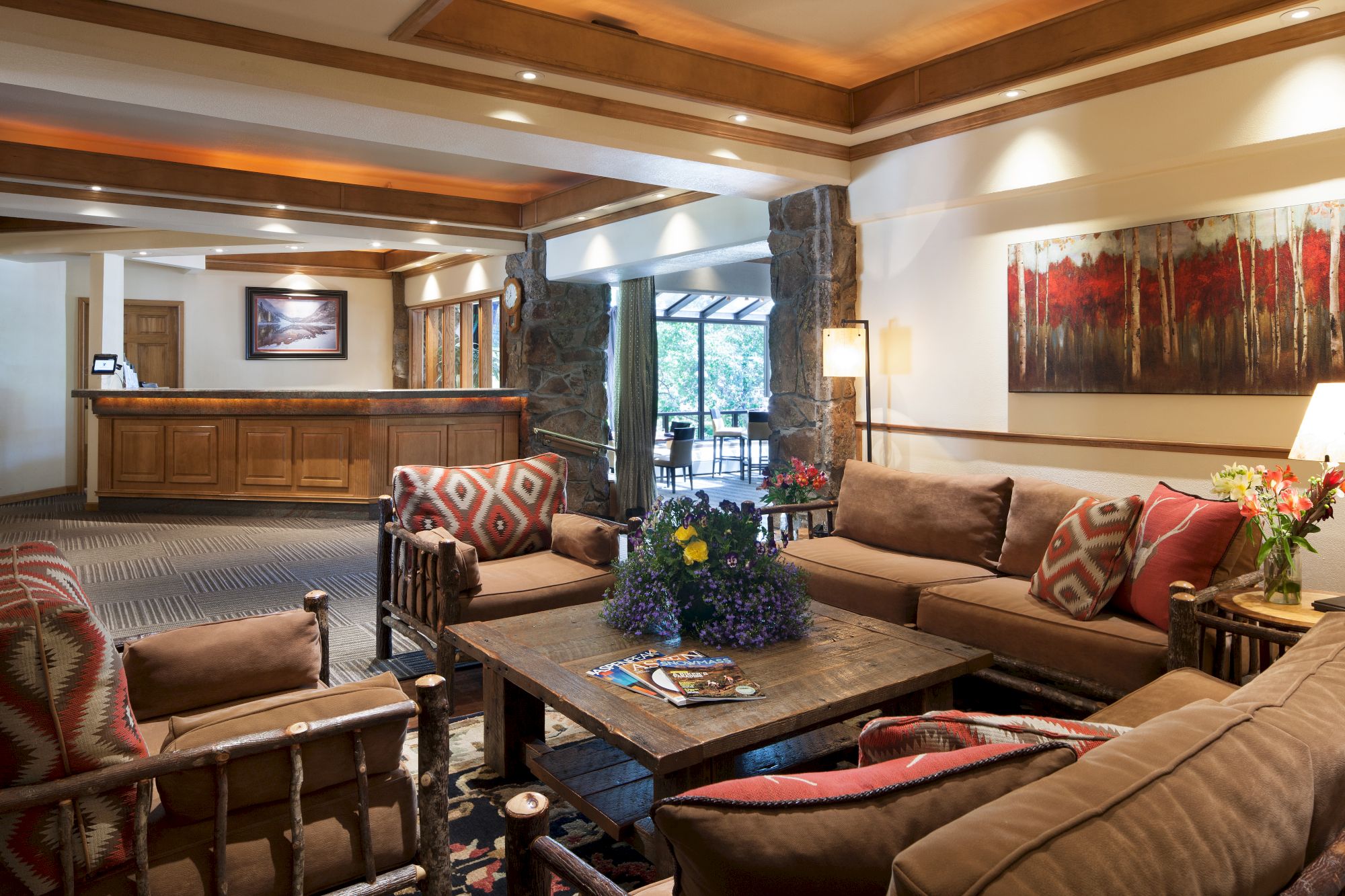 A cozy lobby with comfortable seating, a wooden reception desk, vibrant artwork, and a large coffee table adorned with magazines and flowers.