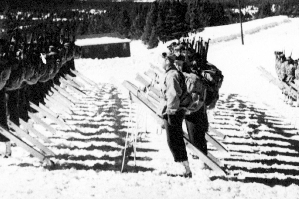 Rows of soldiers in winter gear stand in formation with skis in the snow, seemingly undergoing training or inspection in a snowy landscape.
