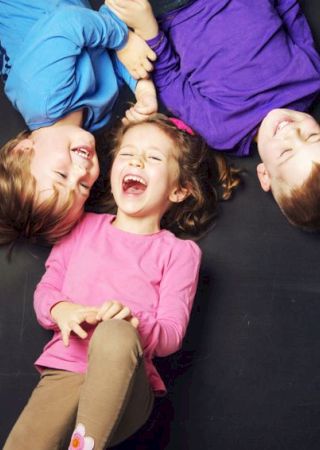 Three children wearing colorful shirts are lying down and laughing together, creating a joyful and playful atmosphere.