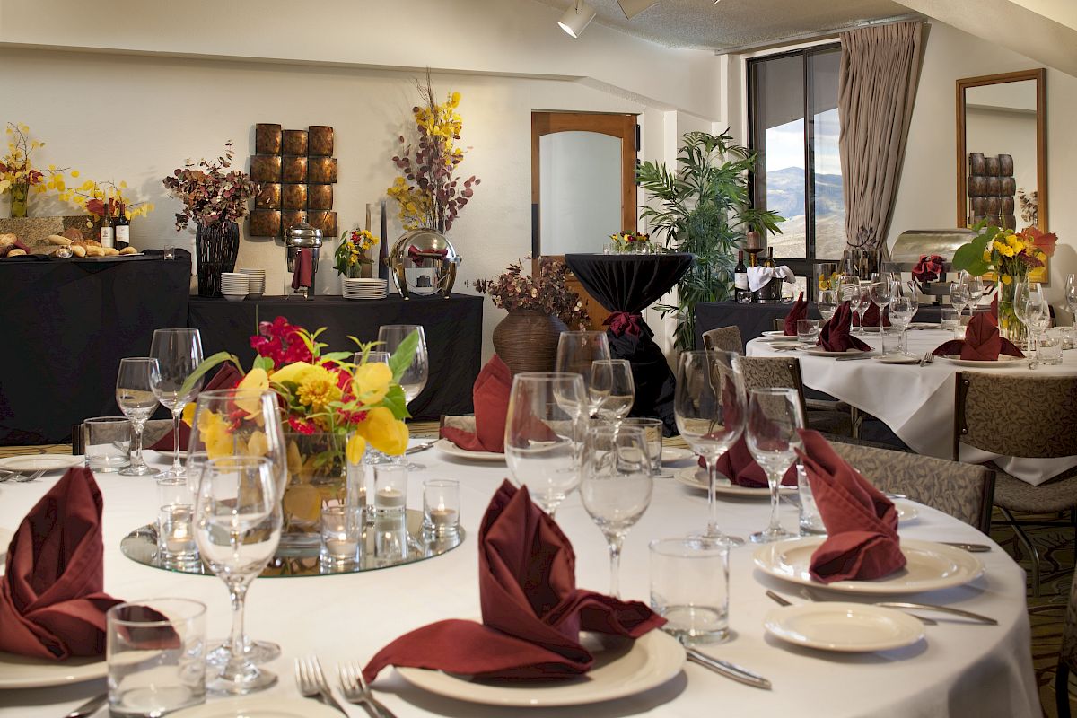 A beautifully set dining table with red napkins, glassware, and floral centerpieces is seen in an elegantly decorated room with buffets and decor.