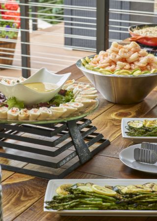 The image features a buffet table with shrimp, asparagus, pasta, and other dishes, along with plates and utensils for serving them.
