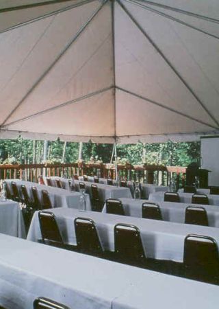 A tented outdoor area is set up classroom-style with rows of tables and chairs, all covered in white tablecloths, along with a podium and projector screen.