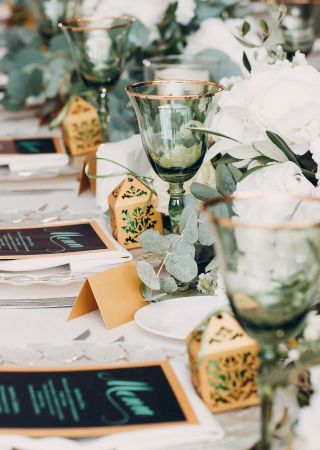 A beautifully set table at a formal event, adorned with green goblets, white flowers, gold gift boxes, menus, and place cards.