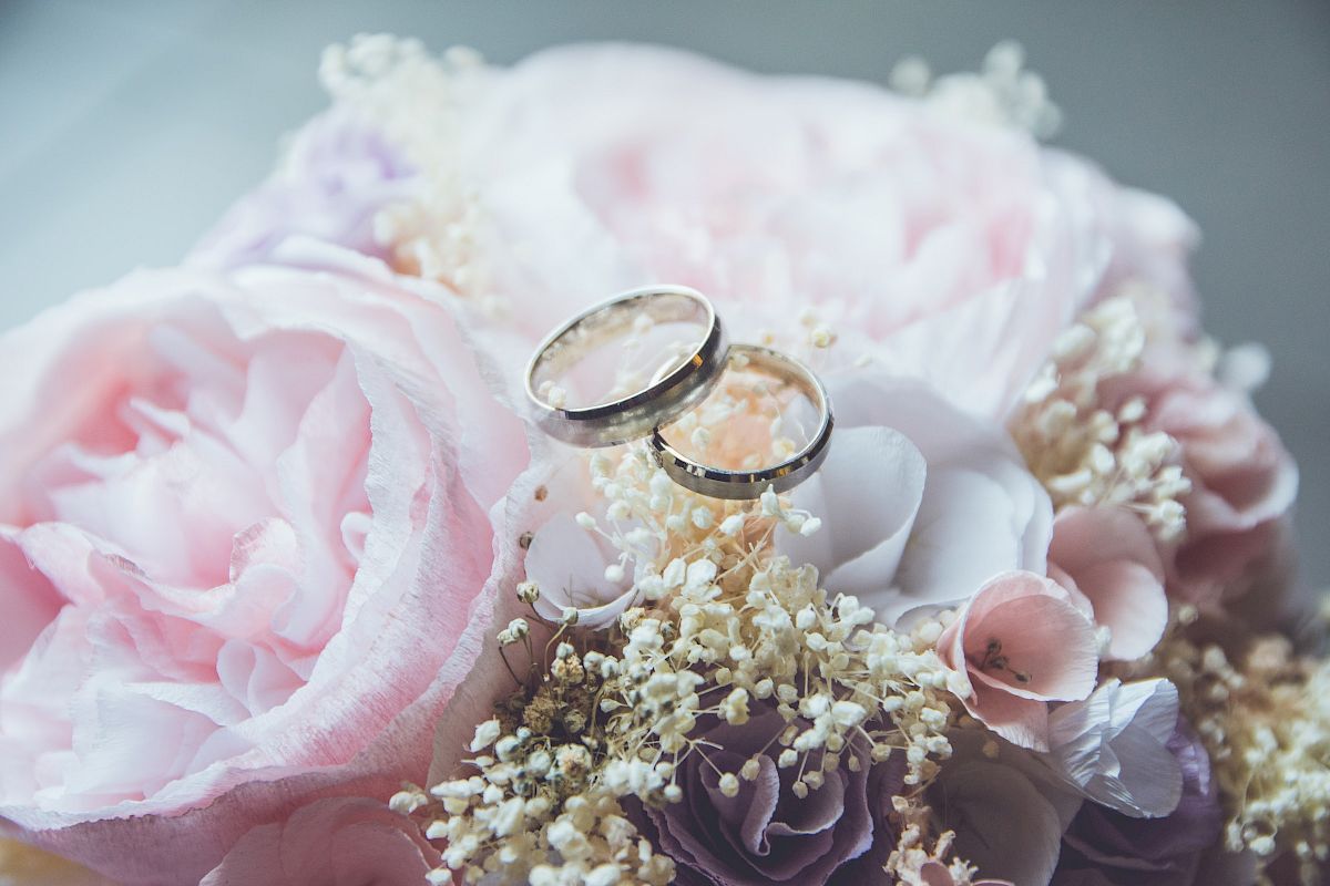 The image shows two wedding rings placed on top of a bouquet of light pink and white flowers, creating a romantic and elegant scene.