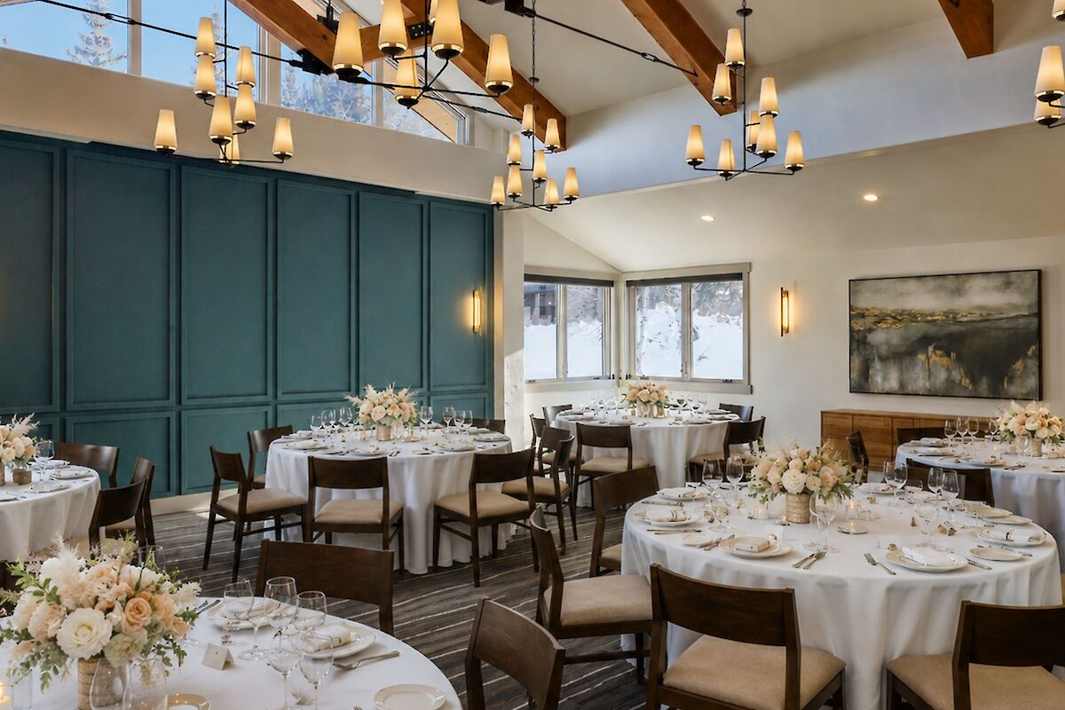 Elegant banquet hall set for a formal event; round tables with white linens and floral centerpieces, soft lighting, and a teal paneled wall.