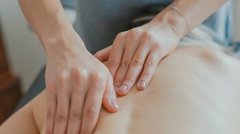 A person is receiving a back massage from another individual, who is using both hands to apply pressure in a kneading motion.