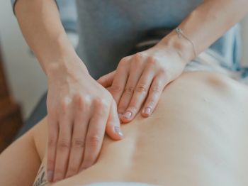 A person is receiving a back massage from another individual, who is using both hands to apply pressure in a kneading motion.
