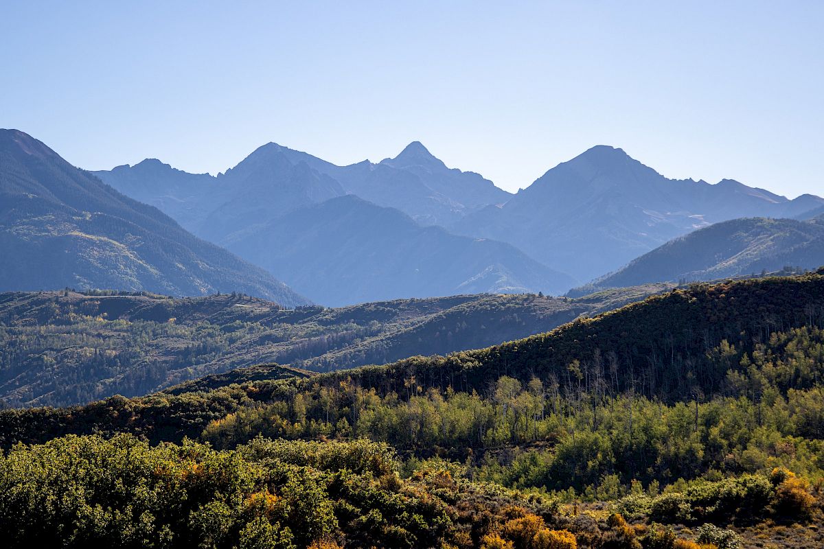 The image shows a beautiful mountain range with lush green vegetation in the foreground under a clear blue sky.
