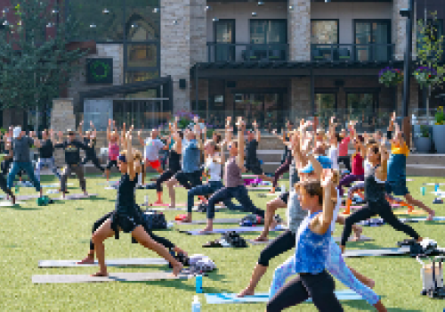 A group of people is participating in an outdoor yoga class on a grassy area in front of a building, practicing various poses together.