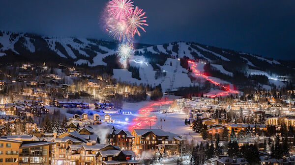 A snowy mountain village with fireworks in the sky and illuminated ski slopes create a vibrant nighttime scene.