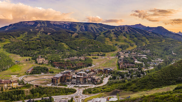 A scenic landscape with mountains, a valley, and a town nestled among trees, under a vibrant sunset sky with scattered clouds.