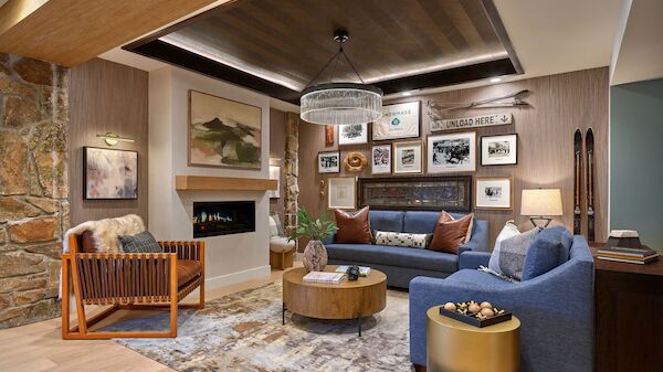 A cozy living room with a blue sectional sofa, a wooden coffee table, gallery wall, stone accent wall, fireplace, plush rug, and warm lighting.