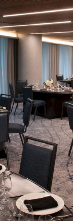 The image shows a banquet hall with round tables set for an event, featuring elegant place settings, candles, and floral centerpieces.